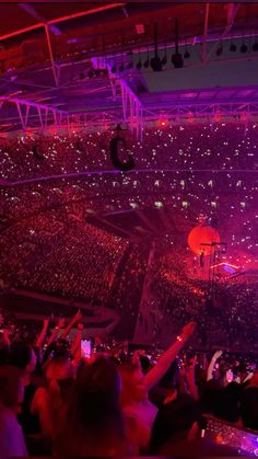 a large crowd at a concert with their hands up in the air and lights on