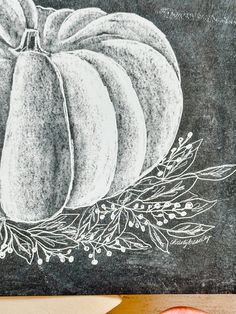 a chalkboard with a drawing of a pumpkin and leaves on it next to a cutting board