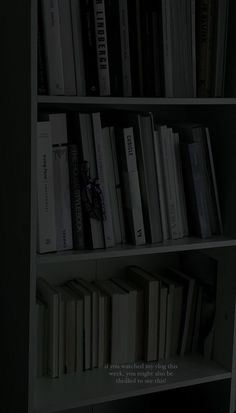 a bookshelf filled with lots of books next to a wall mounted clock in a dark room