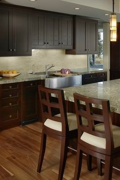 a kitchen with dark wood cabinets and marble counter tops, along with wooden flooring