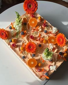 a square cake with oranges, blueberries and flowers on it sitting on a white plate