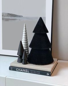 three black and white christmas trees sitting on top of a shelf next to a book