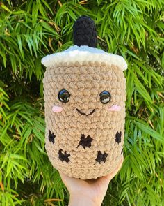 a hand holding up a crocheted coffee cup with a face on the top