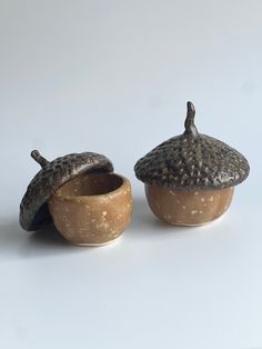 two small ceramic pots with lids on each one and an acorn in the middle