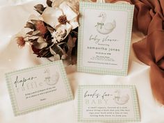 three baby shower cards sitting on top of a bed next to a bouquet of flowers