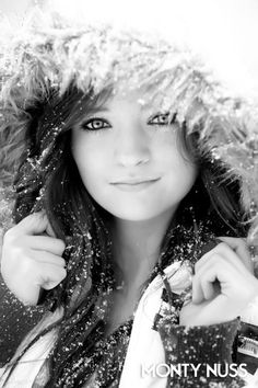 a beautiful young woman wearing a fur hat in the snow with her hands on her hips