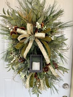 a christmas wreath hanging on the front door with a lit candle and greenery around it