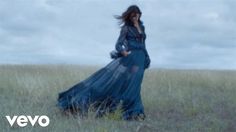 a woman in a long blue dress walking through tall grass