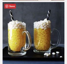 two mugs filled with white and yellow candy on top of a black tray next to each other