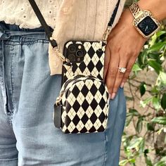 a woman is holding her cell phone in her hand while wearing a black and white checkered purse