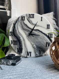 a marble clock sitting on top of a table next to a plant and a camera