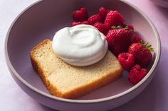 a bowl filled with bread and strawberries on top of a pink tablecloth next to a cup of yogurt