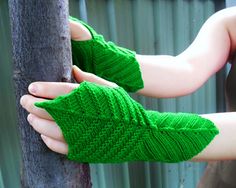 a person wearing green knitted mitts on their hands next to a tree trunk