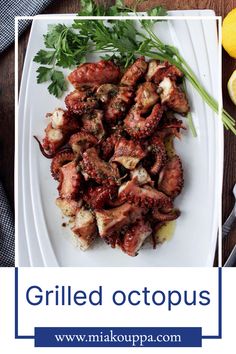 grilled octopus on a white plate with lemons and parsley next to it