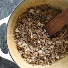 ground beef and onions cooking in a pot with a wooden spoon on the stove top