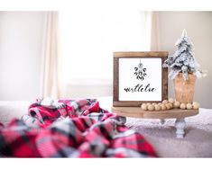 a wooden sign sitting on top of a bed next to a christmas tree and other decorations