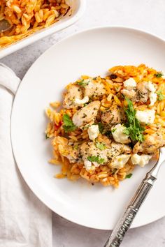 a white plate topped with chicken and rice next to a bowl of pasta salad on a table