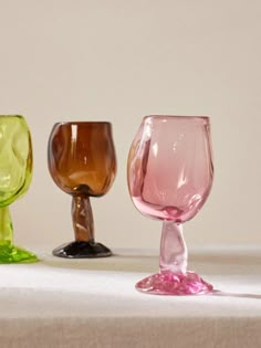 three different colored glass goblets sitting on a white tablecloth covered table cloth