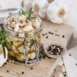 a jar filled with pickled up vegetables on top of a wooden cutting board next to garlic and pepper