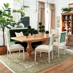 the dining room table is surrounded by white chairs and green couches, along with potted plants