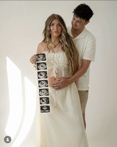 a man and woman standing next to each other in front of a white wall with pictures on it