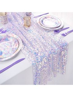 the table is set with plates, silverware and purple sequins on it