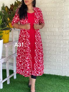 a woman standing in front of a white brick wall wearing a red floral print dress