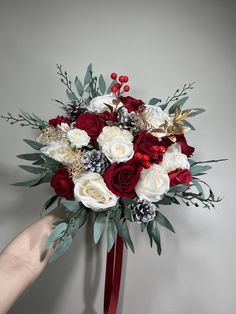 a bridal bouquet with red and white flowers is being held by a woman's hand