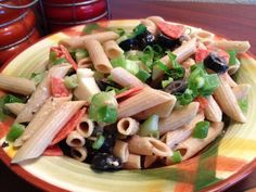 pasta salad with olives, peppers and other vegetables on a yellow and orange plate