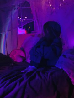 a woman sitting on top of a bed under a purple light