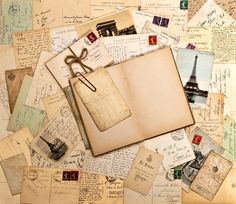 an open book sitting on top of a pile of old letters and postcards with the eiffel tower in the background