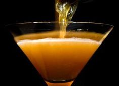 an orange drink being poured into a martini glass on a black background with a spoon in it