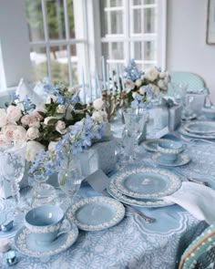 a table set with blue and white plates, silverware and flowers in vases