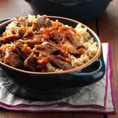 a bowl filled with meat and rice on top of a wooden table next to a pot