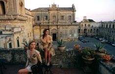 two women sitting on top of a building with potted plants in front of them