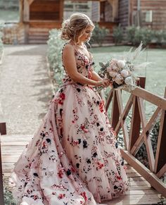 a woman in a floral dress standing on a wooden bridge holding a bouquet and looking at the camera