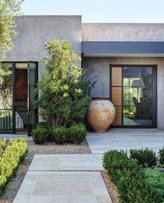 a large vase sitting in the middle of a garden next to a building with glass doors