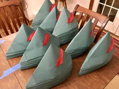 six paper hats with red feathers sitting on top of a wooden table in front of a window