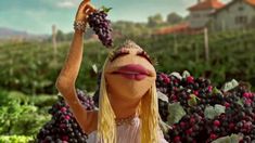 the muppet is holding up grapes in front of her face and wearing a tiara