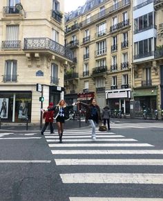 three women crossing the street in front of some tall buildings with balconies on them