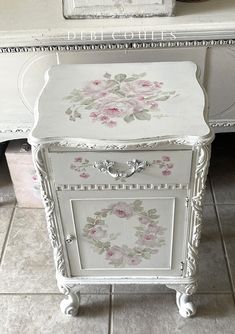 an old dresser painted white with pink flowers on the front and bottom drawers, sitting on tile flooring