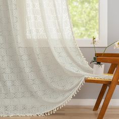 a white lace curtain hanging from a window next to a wooden table with flowers on it