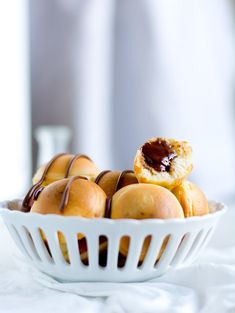 a white bowl filled with mini rolls covered in chocolate sauce and drizzled on top