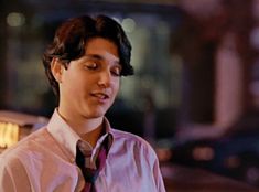 a man wearing a dress shirt and tie standing in front of a building at night