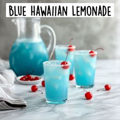 blue hawaiian lemonade with cherries in front of pitcher and glasses on marble table