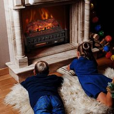 two children sitting on the floor in front of a fireplace