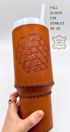 a hand holding a leather cup sleeve with the flower of life engraved on it's side