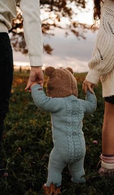 two people holding hands while standing in grass with a teddy bear on one hand and another person's leg behind them