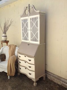 a white dresser sitting next to a chair on top of a dirt floor in front of a wall