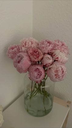 a vase filled with pink flowers sitting on top of a white table next to a wall